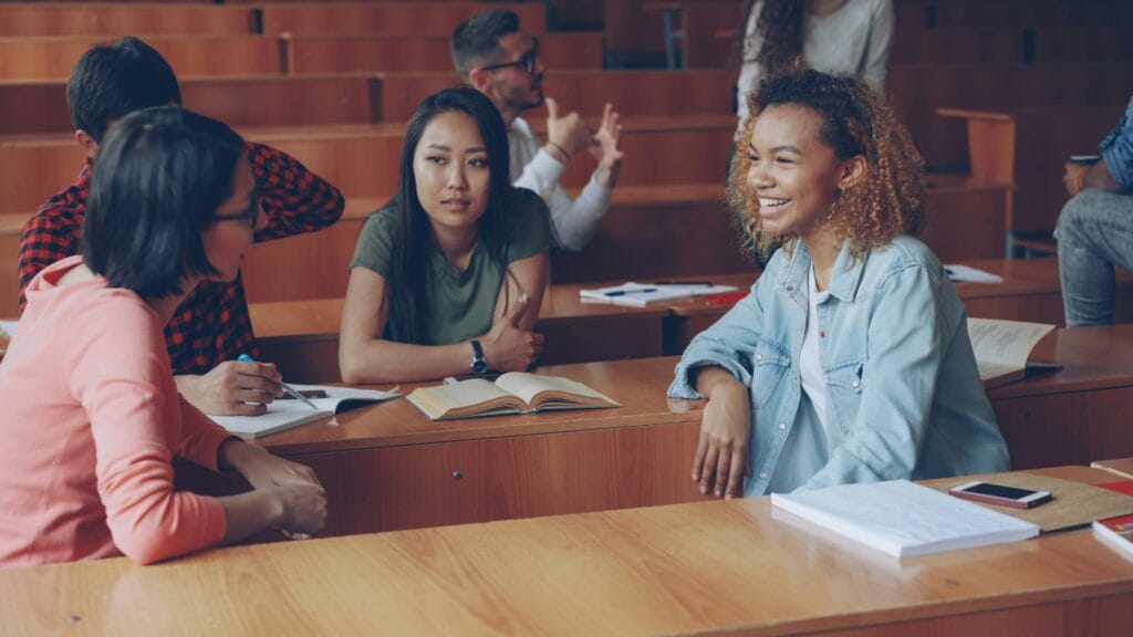 Three students practising English conversation together at a classroom desk