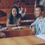 Three students practising English conversation together at a classroom desk
