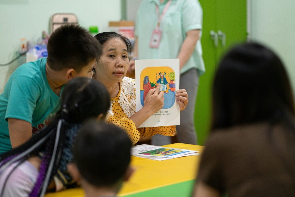 Teacher holding up a picture card to young learners around a classroom table