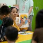 Teacher holding up a picture card to young learners around a classroom table