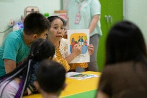 Teacher holding up a picture card to young learners around a classroom table