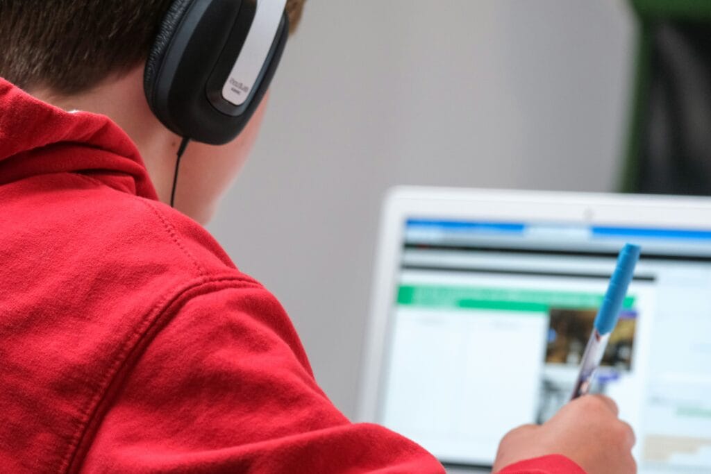 Student in headphones reading an article on a laptop while taking notes