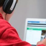 Student in headphones reading an article on a laptop while taking notes