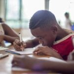 Two young children writing in notebooks with pencils at a desk